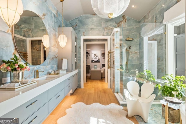 bathroom with hardwood / wood-style floors, vanity, lofted ceiling, tile walls, and a shower with shower door