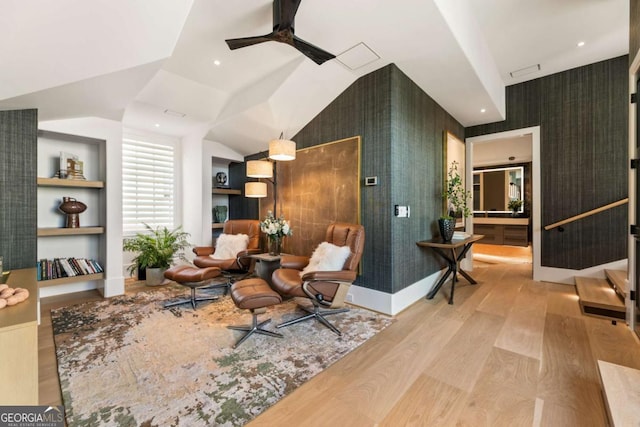 sitting room featuring built in shelves, ceiling fan, light wood-type flooring, and lofted ceiling