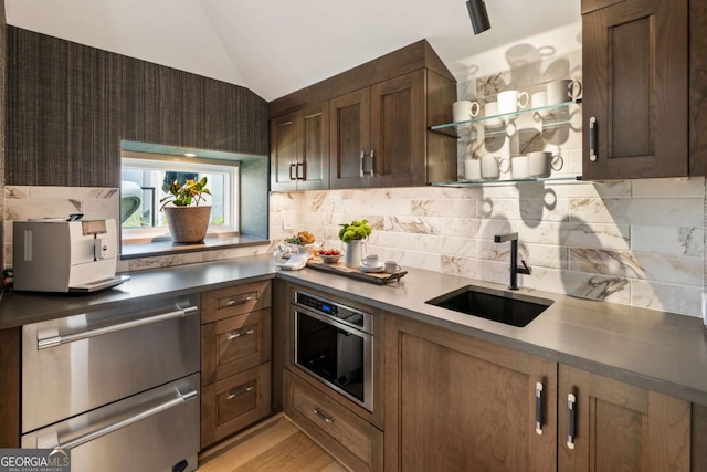 kitchen with light wood-type flooring, backsplash, stainless steel oven, vaulted ceiling, and sink