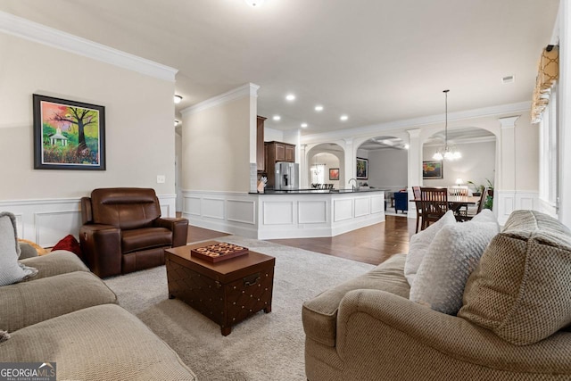 living room with sink, crown molding, light wood-type flooring, a notable chandelier, and decorative columns