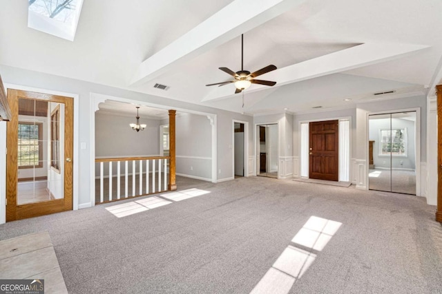 unfurnished living room featuring lofted ceiling with skylight, light colored carpet, ceiling fan with notable chandelier, and ornamental molding