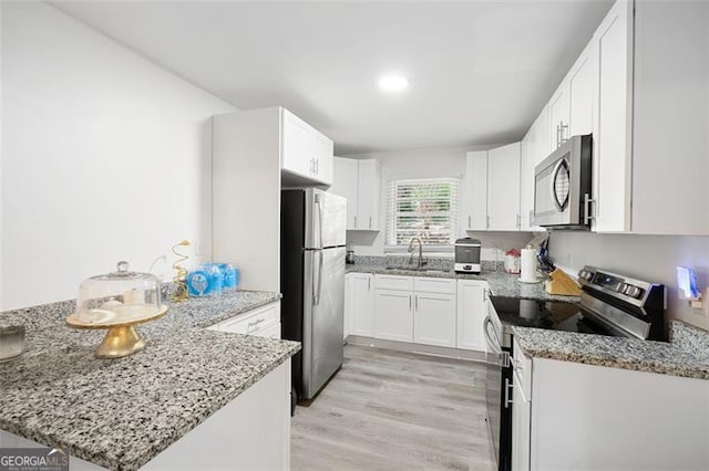 kitchen with light stone countertops, sink, stainless steel appliances, kitchen peninsula, and white cabinets