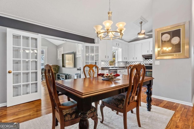 dining space featuring ceiling fan with notable chandelier, light hardwood / wood-style floors, and vaulted ceiling