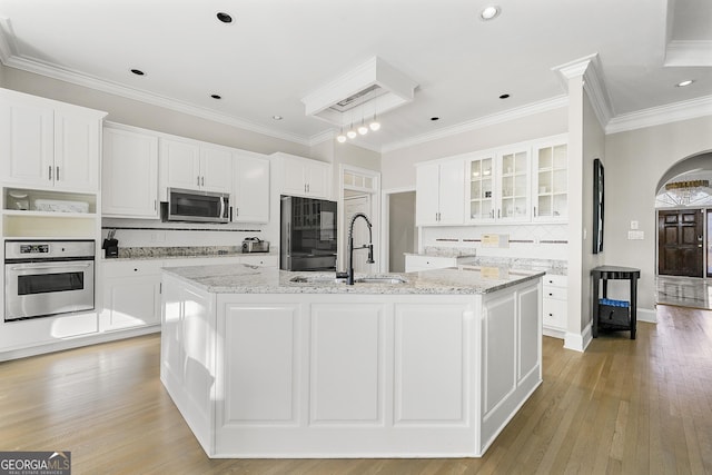 kitchen with appliances with stainless steel finishes, white cabinets, light stone counters, and an island with sink