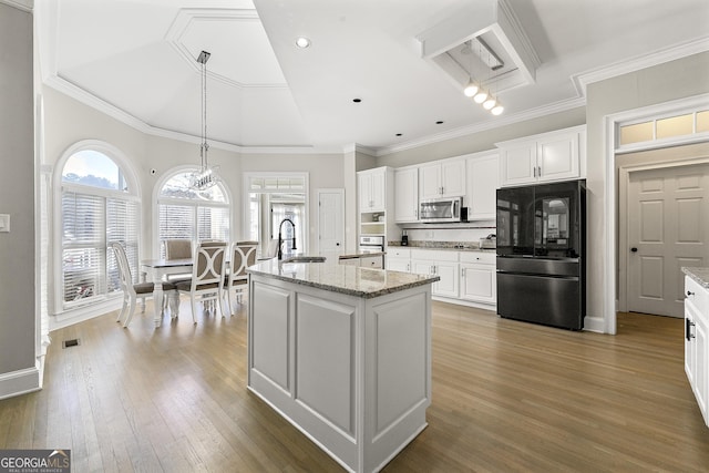 kitchen with light stone counters, white cabinetry, black fridge, and a kitchen island with sink