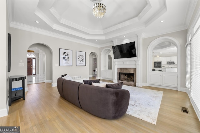 living room featuring a tile fireplace, a tray ceiling, and ornamental molding