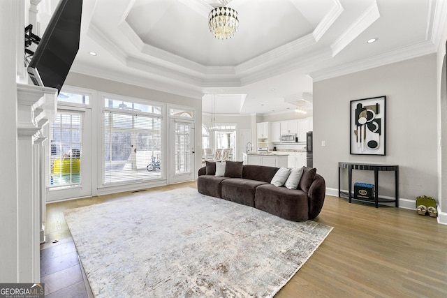 living room featuring a chandelier, light hardwood / wood-style flooring, a raised ceiling, and ornamental molding