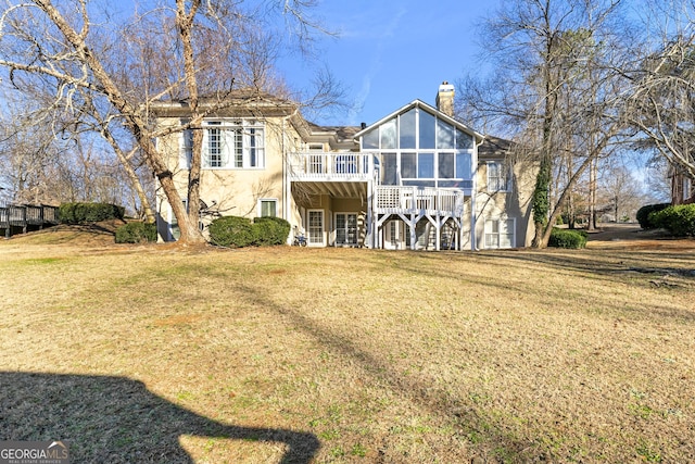 rear view of property featuring a wooden deck, a sunroom, and a lawn