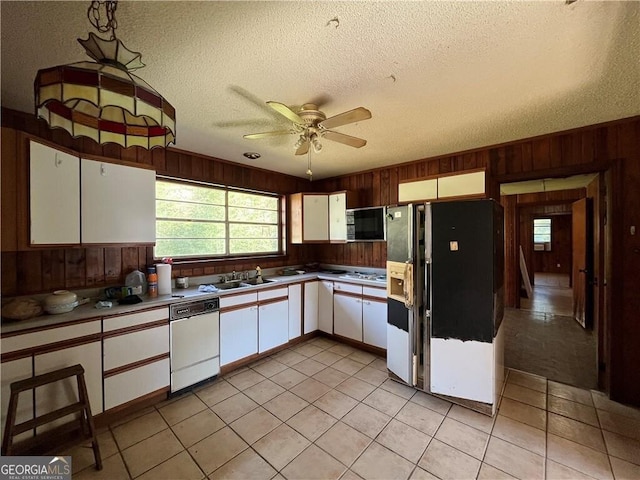 kitchen with white appliances, white cabinets, wooden walls, light tile patterned floors, and a textured ceiling