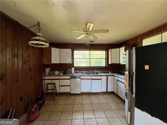 kitchen featuring a textured ceiling, wooden walls, white refrigerator, white cabinets, and light tile patterned flooring