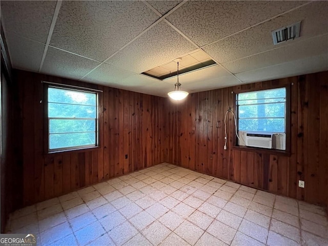 unfurnished room with a wealth of natural light, a drop ceiling, cooling unit, and wood walls