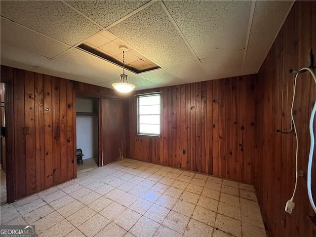 unfurnished bedroom featuring a drop ceiling, a closet, and wooden walls