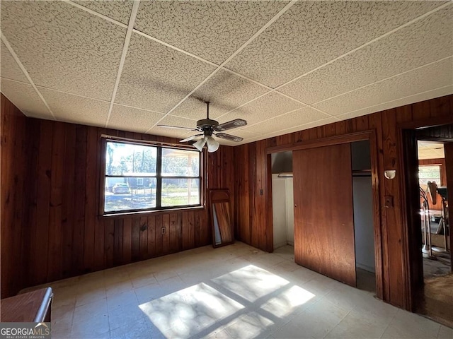 unfurnished bedroom featuring a paneled ceiling, ceiling fan, and wooden walls