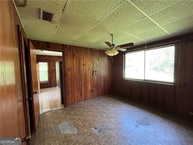 unfurnished room featuring a paneled ceiling, wooden walls, ceiling fan, and a healthy amount of sunlight