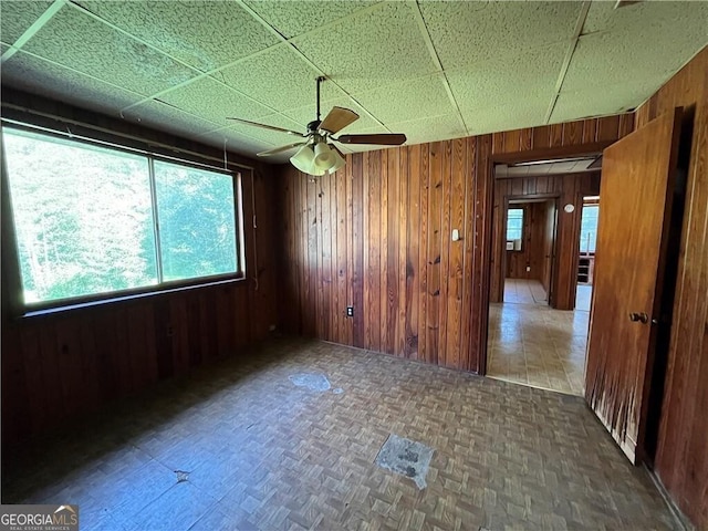 spare room featuring a paneled ceiling, wooden walls, dark parquet floors, and ceiling fan