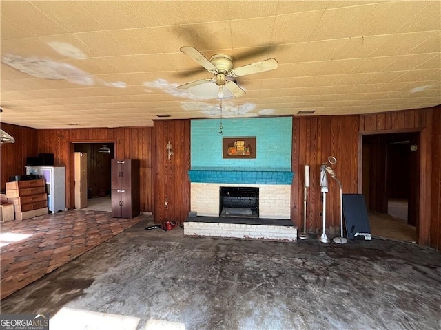 unfurnished living room featuring wooden walls, ceiling fan, and a brick fireplace