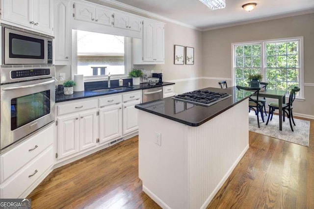 kitchen featuring appliances with stainless steel finishes, a kitchen island, sink, hardwood / wood-style flooring, and white cabinetry