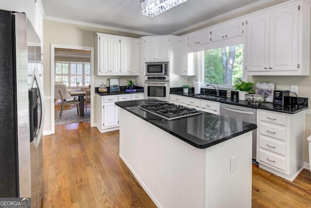 kitchen with appliances with stainless steel finishes, sink, light hardwood / wood-style flooring, white cabinets, and a kitchen island