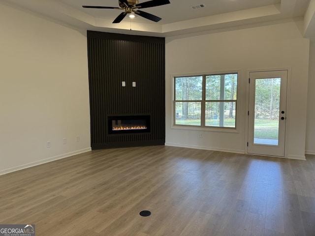 unfurnished living room featuring visible vents, ceiling fan, wood finished floors, and a raised ceiling