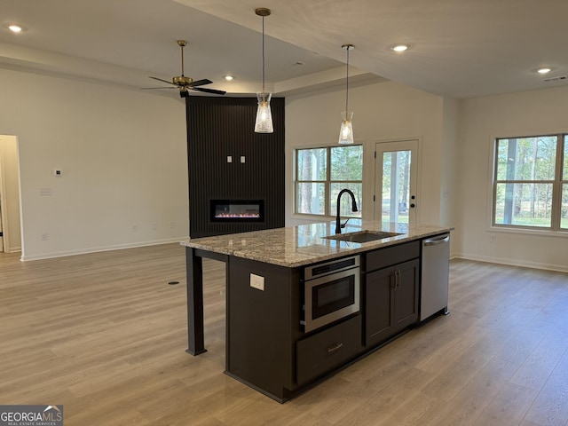 kitchen with open floor plan, a sink, ceiling fan, light wood-style flooring, and appliances with stainless steel finishes