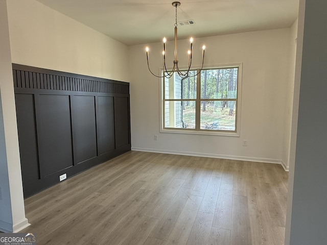 unfurnished dining area featuring wood finished floors, a notable chandelier, baseboards, and visible vents
