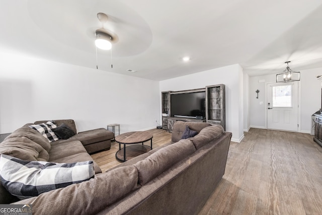 living room featuring ceiling fan with notable chandelier and light wood-type flooring