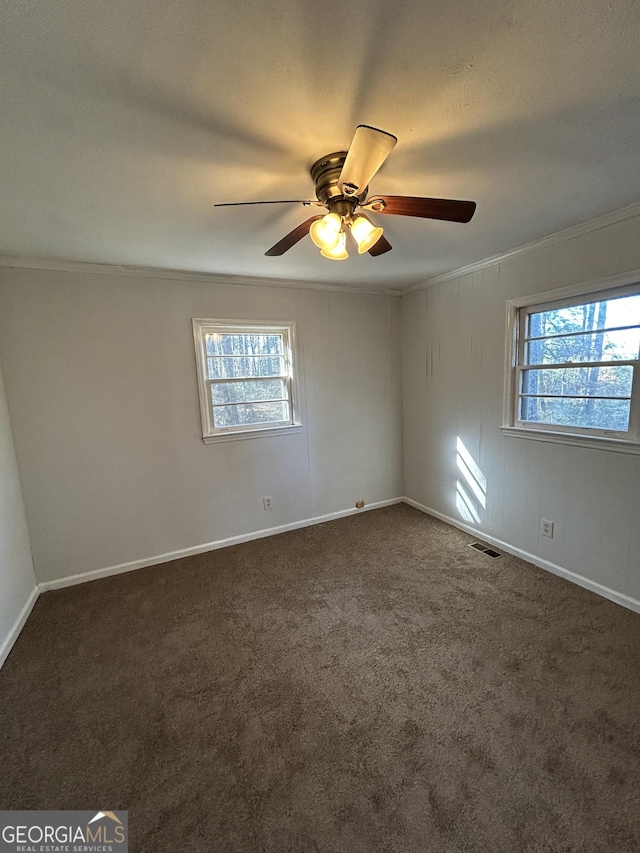 empty room with baseboards, visible vents, dark colored carpet, and crown molding