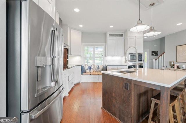 kitchen featuring white cabinets, hanging light fixtures, decorative backsplash, an island with sink, and stainless steel appliances