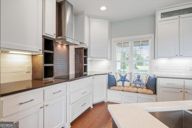 kitchen featuring white cabinetry, wall chimney range hood, dark stone countertops, black electric stovetop, and light wood-type flooring