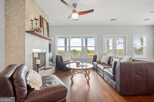 living room with ceiling fan, a large fireplace, wood-type flooring, and french doors