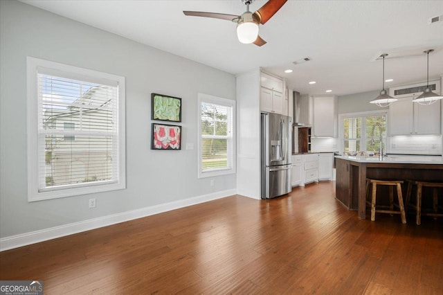 kitchen featuring a kitchen bar, stainless steel refrigerator with ice dispenser, a center island with sink, white cabinetry, and hanging light fixtures