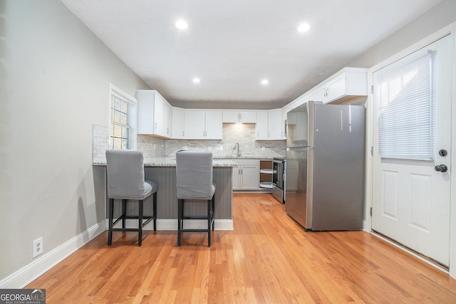 kitchen with sink, a breakfast bar area, white cabinetry, appliances with stainless steel finishes, and light stone countertops