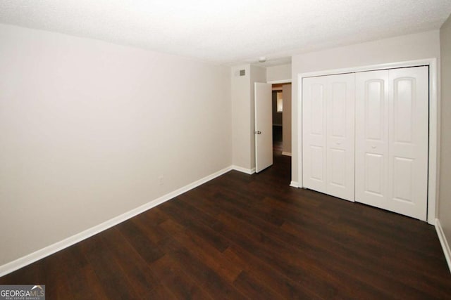 unfurnished bedroom with a textured ceiling, a closet, and dark wood-type flooring