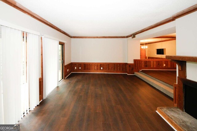 unfurnished living room with crown molding, dark hardwood / wood-style floors, and an inviting chandelier