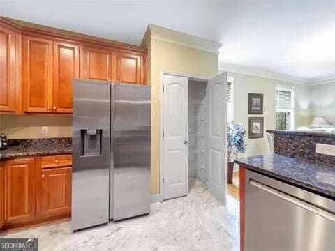 kitchen with ornamental molding, dark stone counters, and appliances with stainless steel finishes