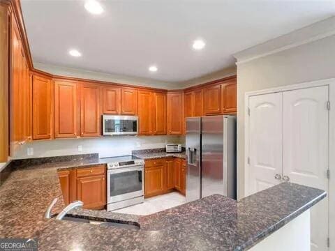 kitchen with sink, kitchen peninsula, stainless steel appliances, and dark stone counters