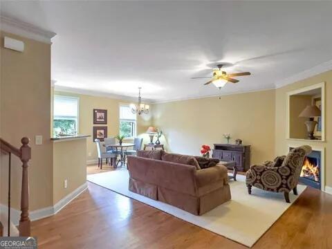 living room with light wood-type flooring, ceiling fan with notable chandelier, and ornamental molding