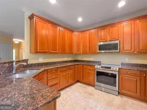 kitchen with kitchen peninsula, dark stone countertops, sink, and stainless steel appliances