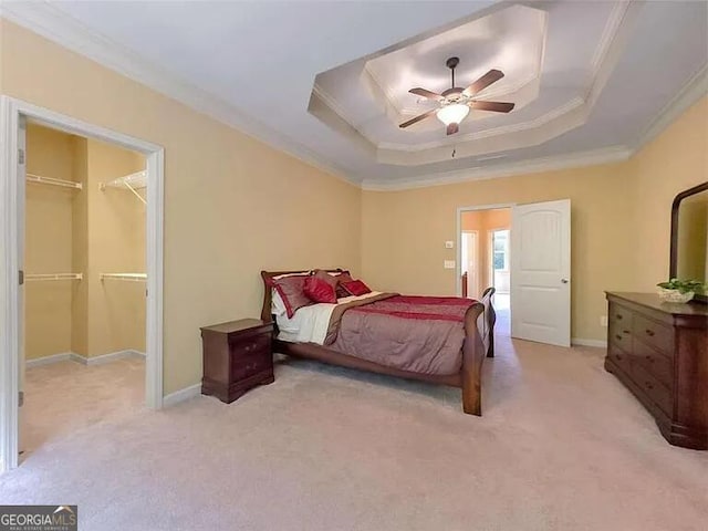 bedroom featuring ceiling fan, a spacious closet, crown molding, and a tray ceiling