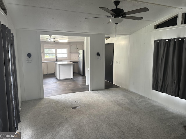 unfurnished living room with carpet flooring, ceiling fan, and vaulted ceiling