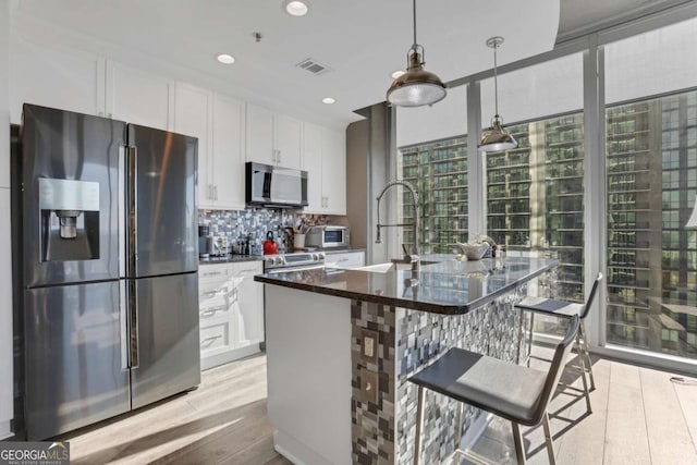 kitchen with sink, white cabinetry, stainless steel appliances, and an island with sink