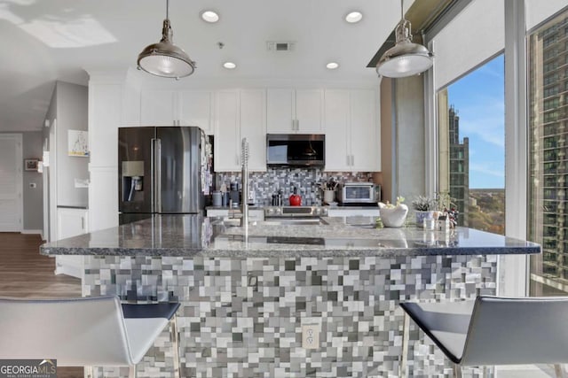 kitchen featuring appliances with stainless steel finishes, white cabinetry, hanging light fixtures, and dark stone counters