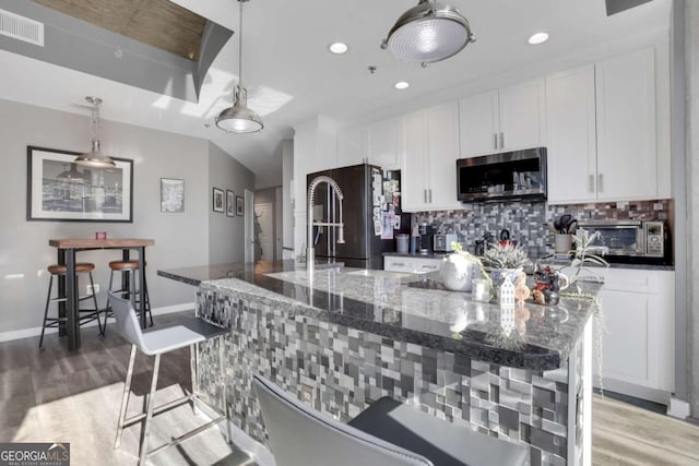 kitchen with decorative backsplash, high quality fridge, dark stone counters, a kitchen island with sink, and decorative light fixtures