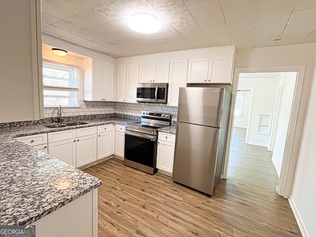 kitchen featuring stone counters, sink, light hardwood / wood-style floors, white cabinets, and appliances with stainless steel finishes