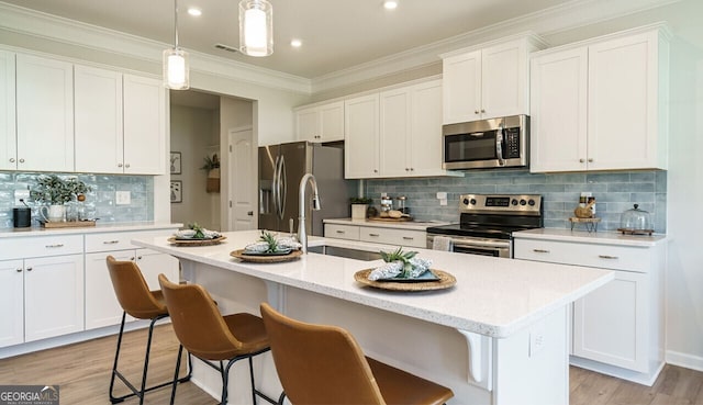 kitchen with backsplash, a kitchen island with sink, white cabinets, hanging light fixtures, and appliances with stainless steel finishes