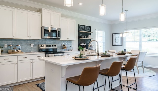 kitchen featuring hanging light fixtures, white cabinetry, a kitchen island with sink, and appliances with stainless steel finishes