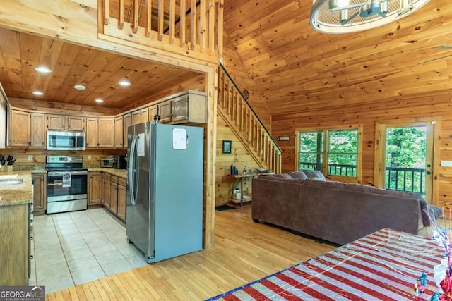 kitchen featuring wooden walls, high vaulted ceiling, light stone counters, and appliances with stainless steel finishes