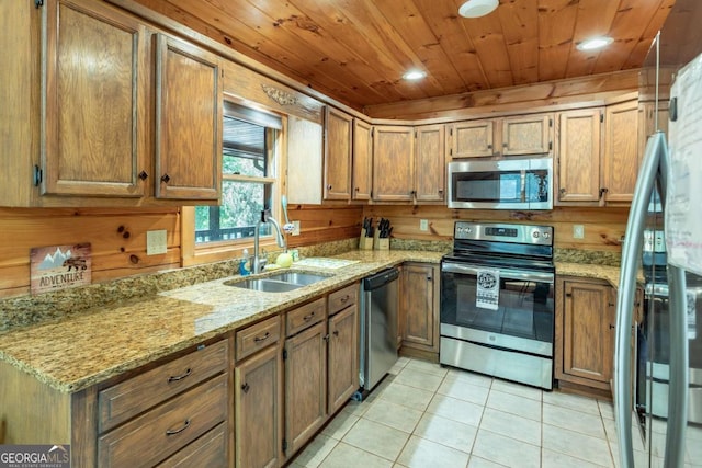 kitchen with sink, wooden walls, appliances with stainless steel finishes, light tile patterned flooring, and light stone counters