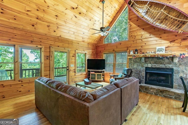 living room featuring a fireplace, light wood-type flooring, high vaulted ceiling, and wood walls