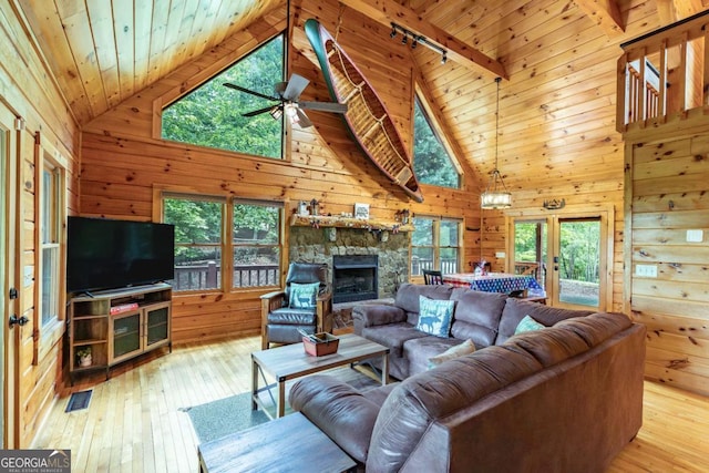 living room with track lighting, high vaulted ceiling, wooden walls, and light hardwood / wood-style flooring